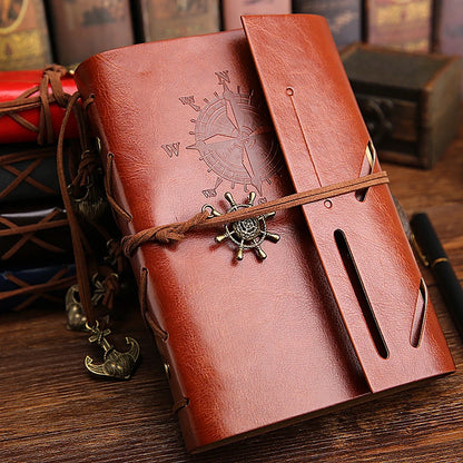 Brown leather notebook with ship wheel charm on a wooden surface