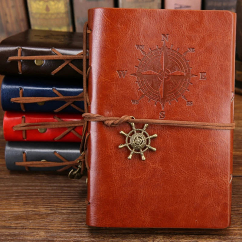 Brown leather notebook with compass and ship wheel design, tied with brown string, on a wooden surface.