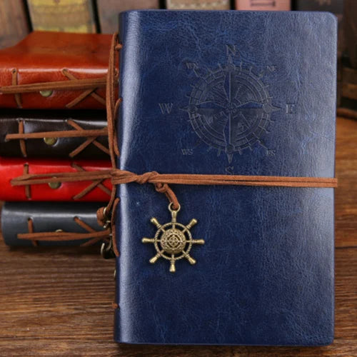 Blue leather notebook with compass and ship wheel design, tied with brown string, on a wooden surface.