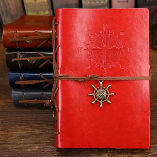 Red leather notebook with compass design and steering wheel charm on a wooden surface.