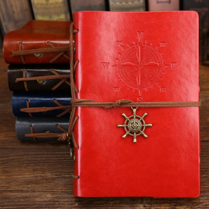 Red leather notebook with compass design and steering wheel charm on a wooden surface.