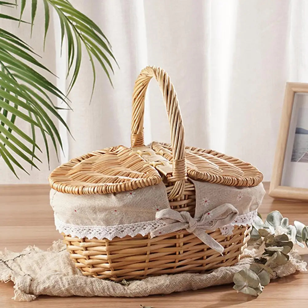Wicker picnic basket with a lid on a wooden surface with a plant and photo frame in the background.